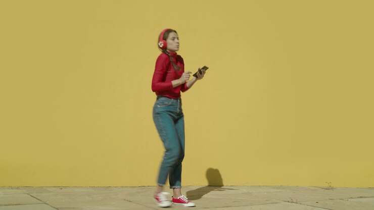 Young Happy Latin Woman wearing red shirt and jeans and red converse shoes starts dancing with a yellow background wall on a sunny day wide-angle shot