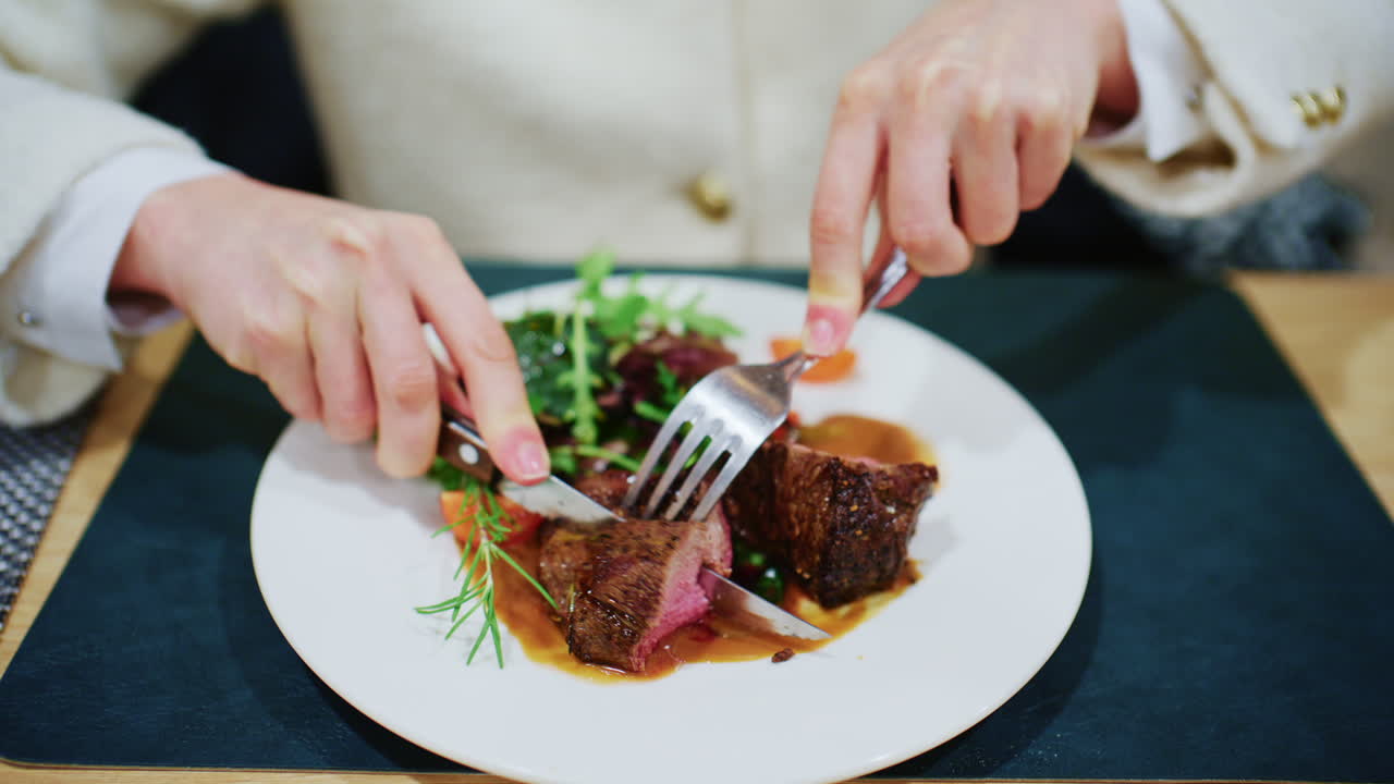 Woman cutting a medium rare steak served with vegetables and sauce on a restaurant plate