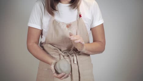 young woman is kneading a clay pieces, shaping balls, close-up of hands