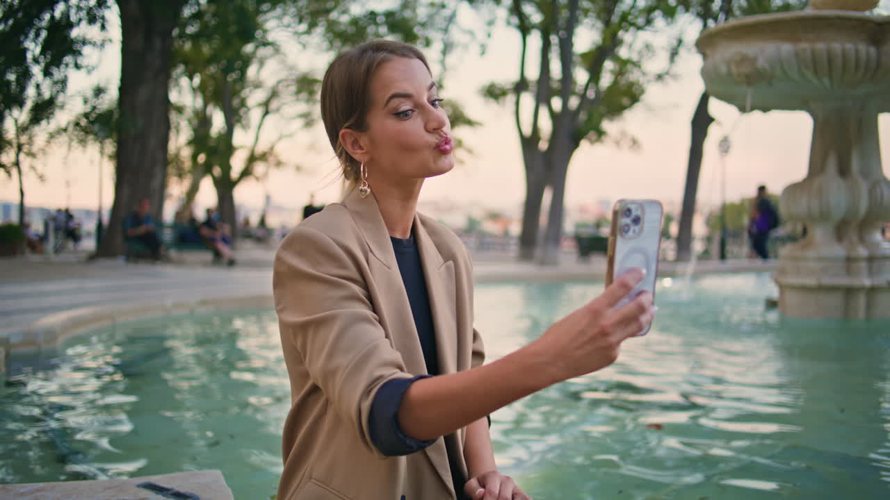 Joyful woman taking selfie video in city park. Beautiful urban girl calling cell