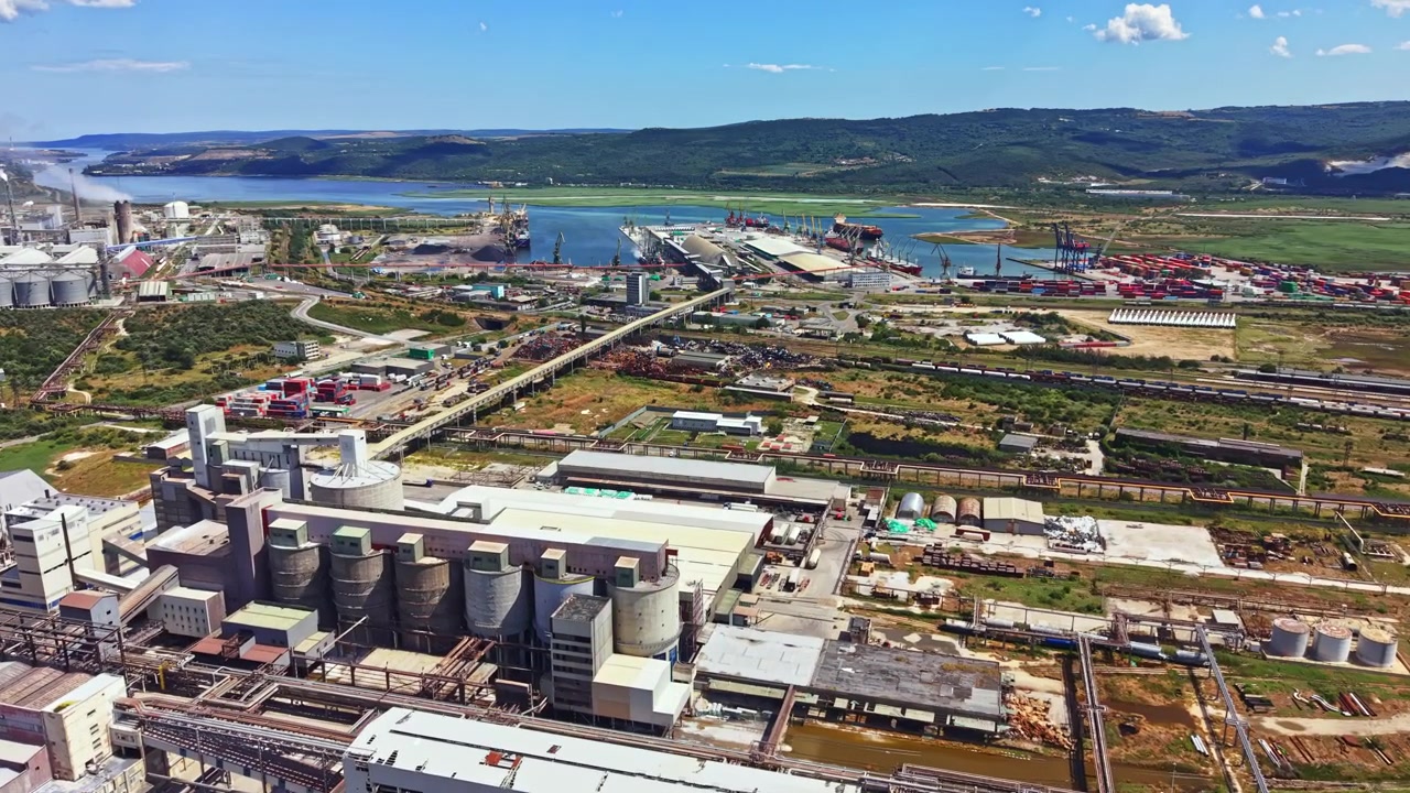 Zona industrial y de transporte cerca de un río con contenedores de carga y edificios durante el día.