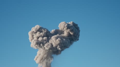 explosion causes mushroom cloud to rises into blue sky in war zone