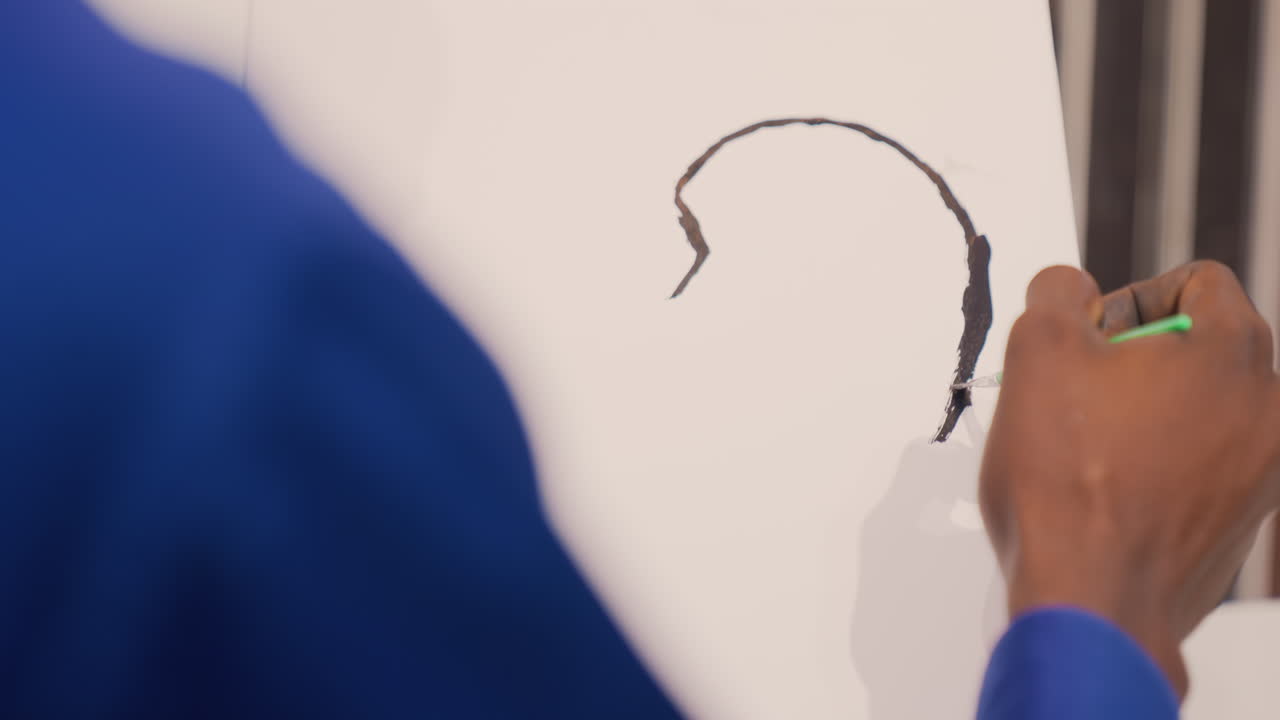 Malíř vytváří jemné kontury fixy. Detail umělce, který jemnými tahy precizně vykresluje obrys ucha na plátno.