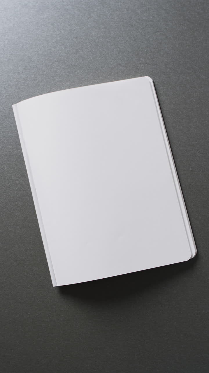 Vertical video of open blank book with copy space on gray background in slow motion