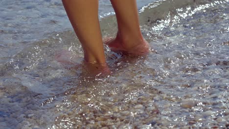 woman wets her feet on the shore of the mediterranean sea on a pebble beach