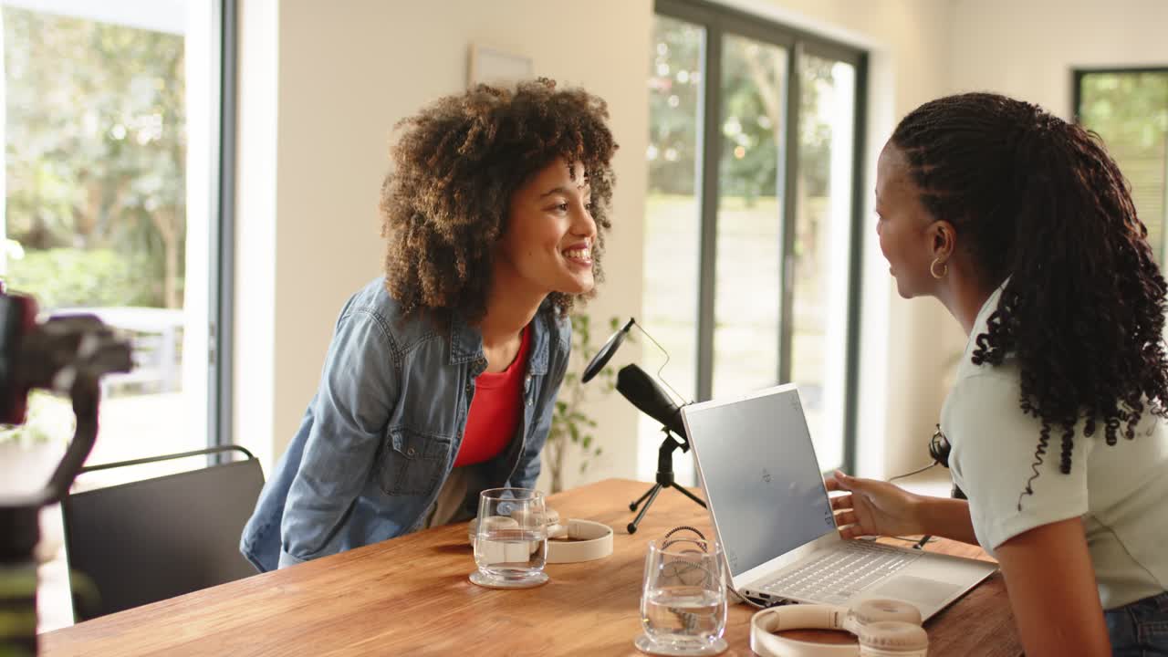 Diverse female coworkers shaking hands before adjusting microphones and recording podcast in studio