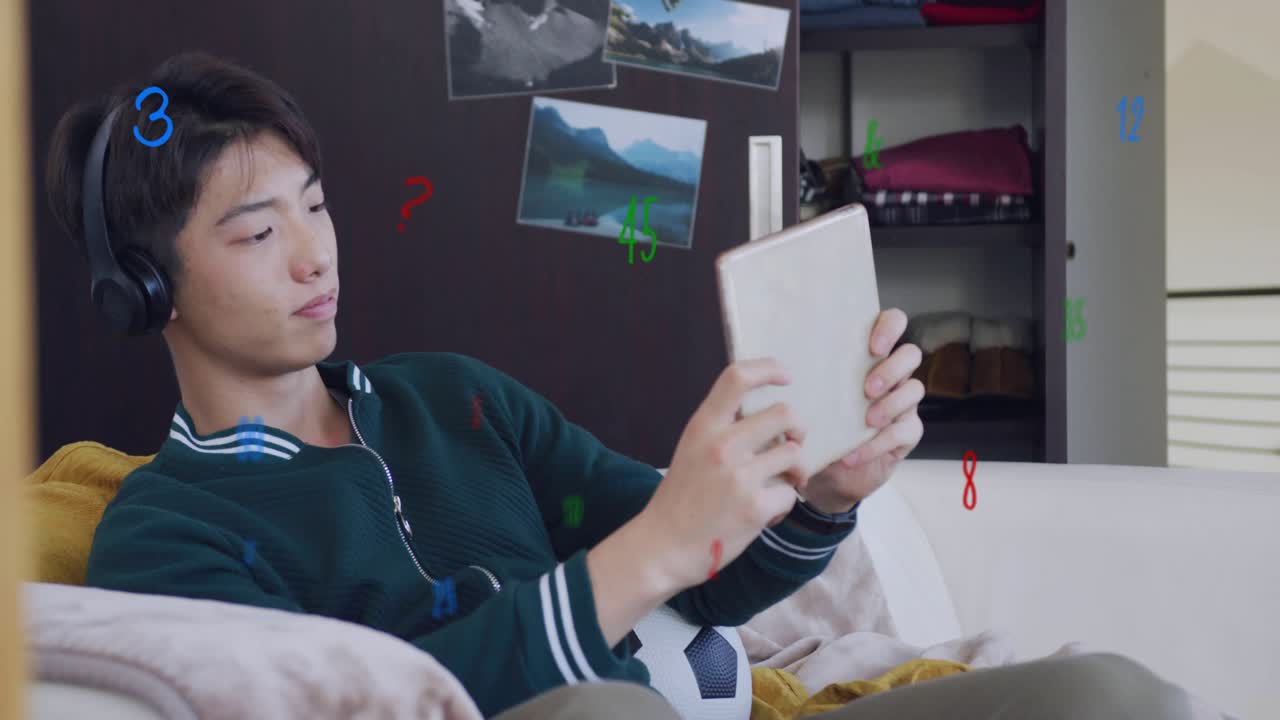 Teen boy reclining on sofa tapping tablet, causing animated numeric graphics for entertainment