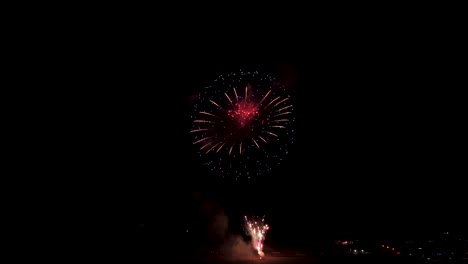 los fuegos artificiales explotan en el cielo nocturno sobre la ciudad durante la celebración del 4 de julio - toma amplia