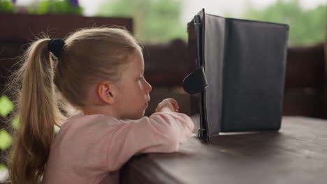 cute little girl watches cartoons online via tablet in cafe