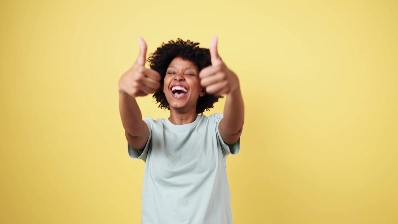 Mulher negra animada fazendo sinal de 'joinha' duplo em fundo amarelo.