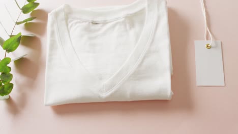 video of close up of white folded t shirt with tag on pink background