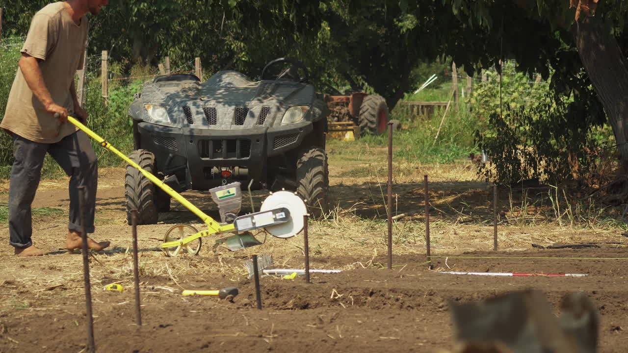 Barefoot farmer using a seeder in his private field, countryman working in the countryside