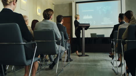 bottom view of caucasian woman in business clothes talking on a podium in a conference room and showing some charts and graphics on the big screen