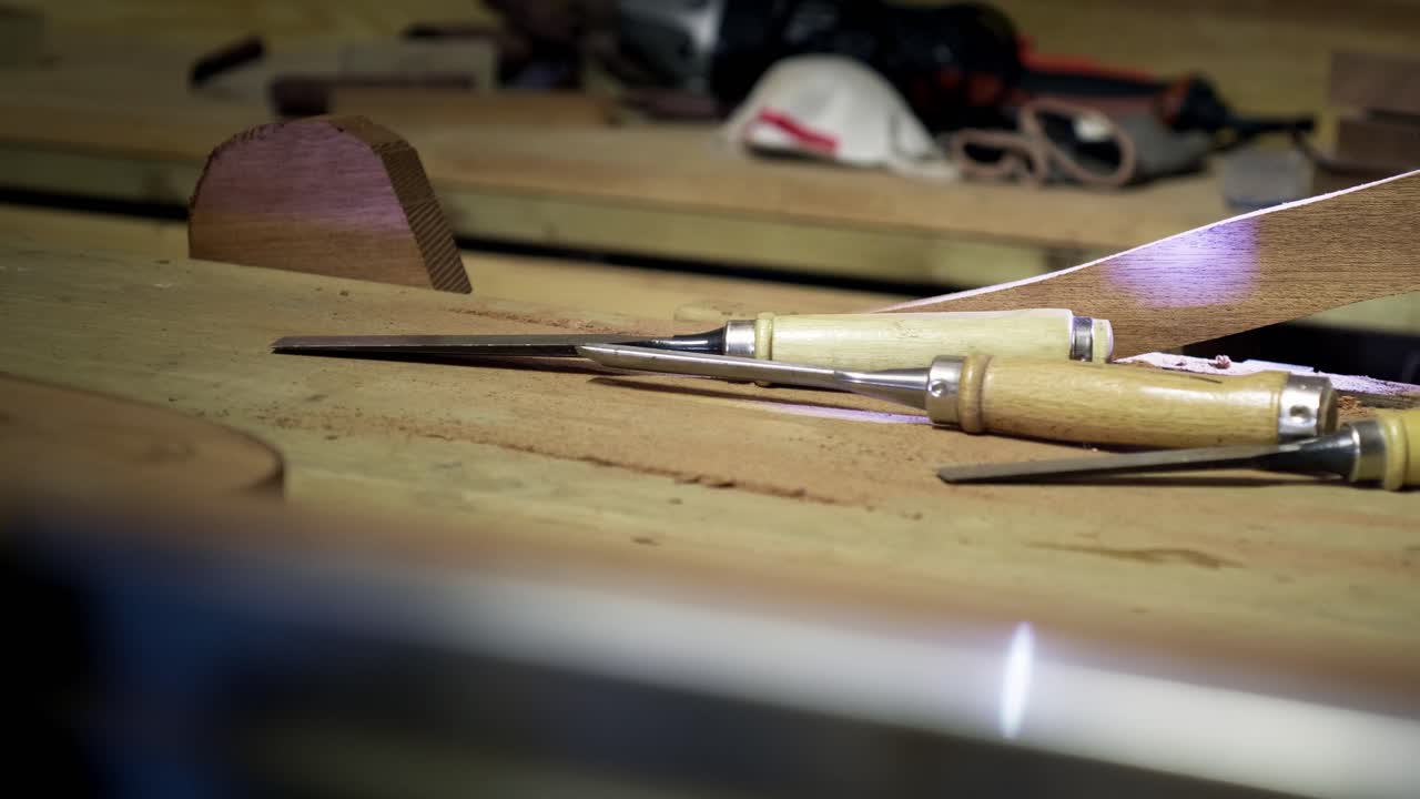 Selection of sharp carving chisels resting on a workbench alongside a partially finished timber project in a carpentry studio. Still life in slow motion
