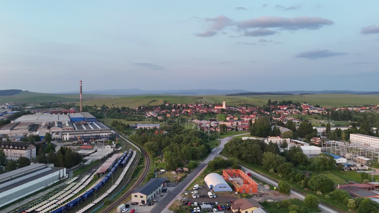 Drone flying backward over Poprad industrial area and residential district, showing railway tracks and countryside in the distance
