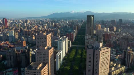 Sobrevuelo-Aéreo-Del-Paisaje-Urbano-De-Taipei-Durante-La-Puesta-De-Sol-Con-Montañas-En-Segundo-Plano.