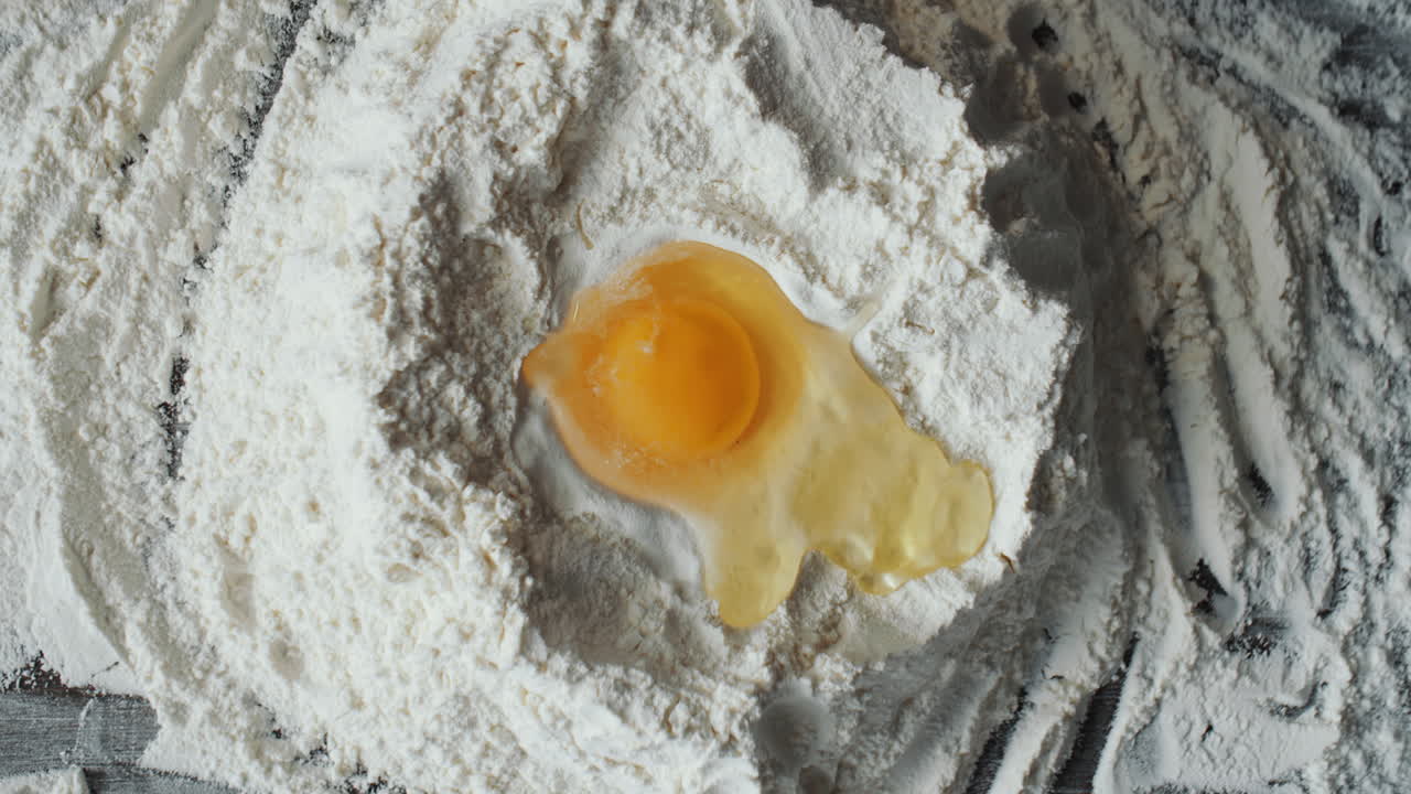Hands Pouring Egg into Well in Center of Flour Mound
