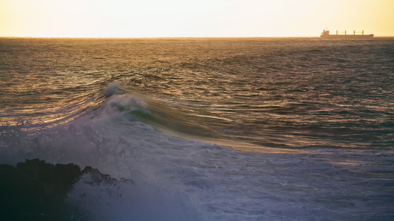 las olas del mar tranquilas rodando hacia la costa rocosa. silueta de barco solitario en el horizonte.