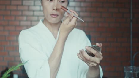 woman applying makeup in a bathrobe