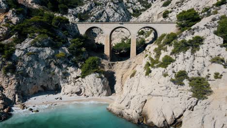 aerial orbit around tall arched bridge crossing white rocks off coast of calanque de l’everine france