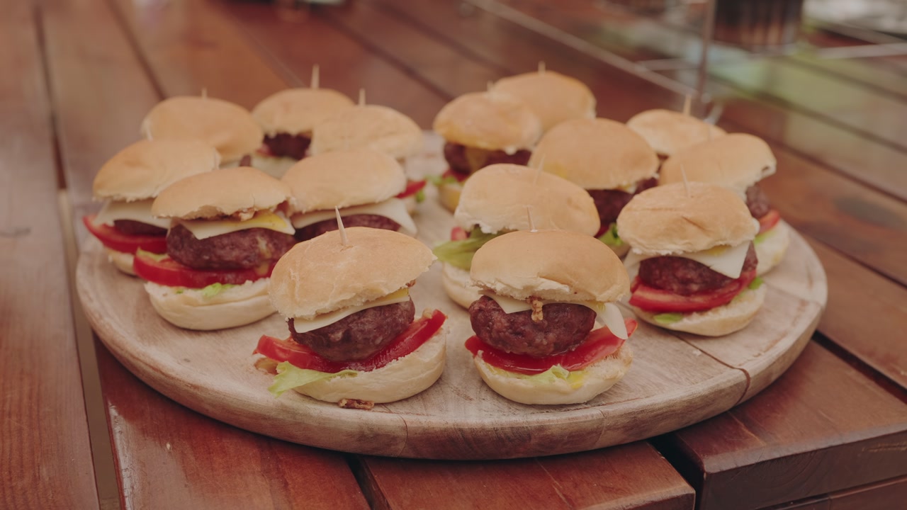 Close up of mini burgers with cheese tomato and lettuce on wooden platter