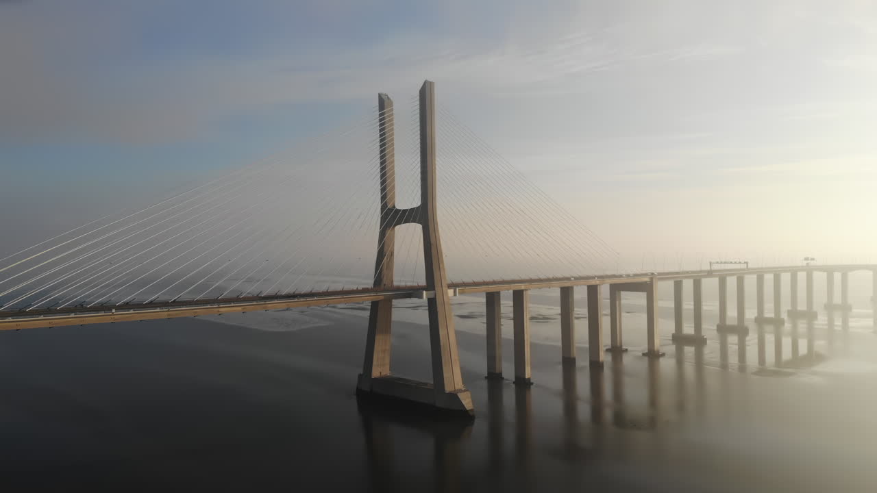 Witness the stunning sunrise illuminating the iconic suspension bridge as calm waters mirror the beautiful colors of the morning sky. This peaceful setting inspires tranquility and awe