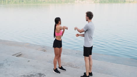 sportive couple warming up and stretching arms near the river