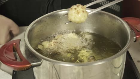 una toma cercana de un chef con las manos agarrando una masa de coliflor frito con pinzas metálicas