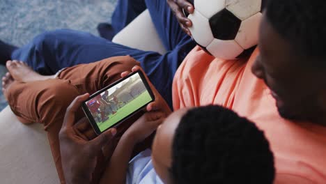 composite of father and son at home watching hockey match on smartphone