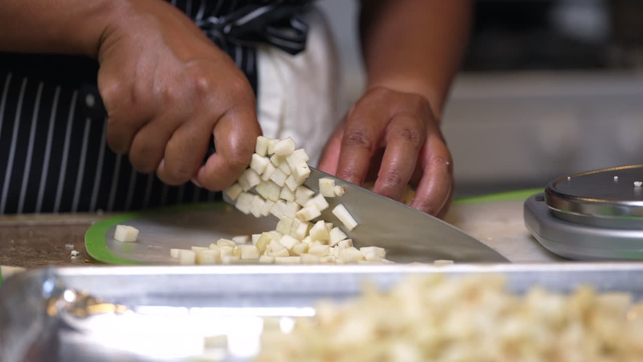 cortando berenjena en cubos en una tabla de cortar - enfóquese en un montón de vegetales picados en una bandeja para hornear