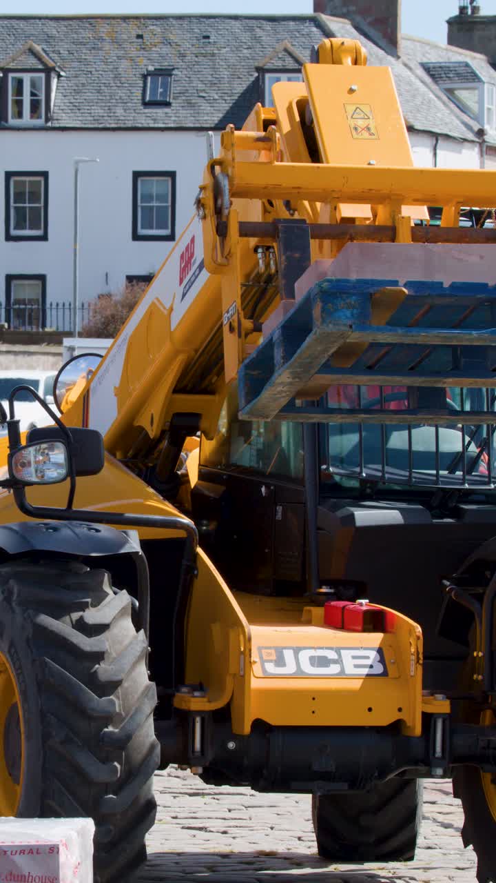 Yellow loader raises pallet in bright daylight, urban street, static camera, clear industrial focus