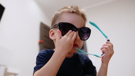 funny caucasian baby boy wearing big black sunglasses. portrait of a cute kid at home. close up.