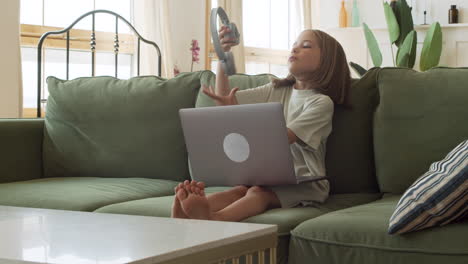 una niña rubia responsable abre la computadora portátil y se pone los auriculares para comenzar su clase en línea desde casa