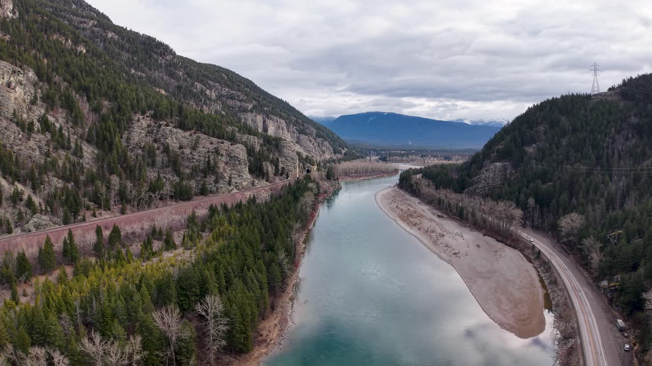 Ripresa aerea con drone dall'alto di un fiume turchese che scorre lungo una valle sinuosa, delimitata da un pendio roccioso con alberi sempreverdi da un lato e una strada sterrata dall'altro nella natura selvaggia vicino a Whitefish