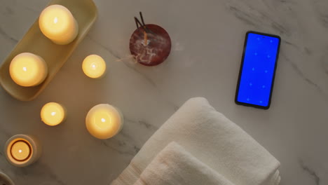 overhead view looking down on still life of blue screen mobile phone with lit candles towels and incense stick as part of relaxing spa day decor