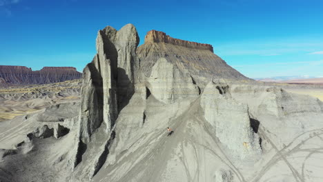 aerial view of man running down the hill, grey sandstone formation in a front of factory butte, utah desert usa