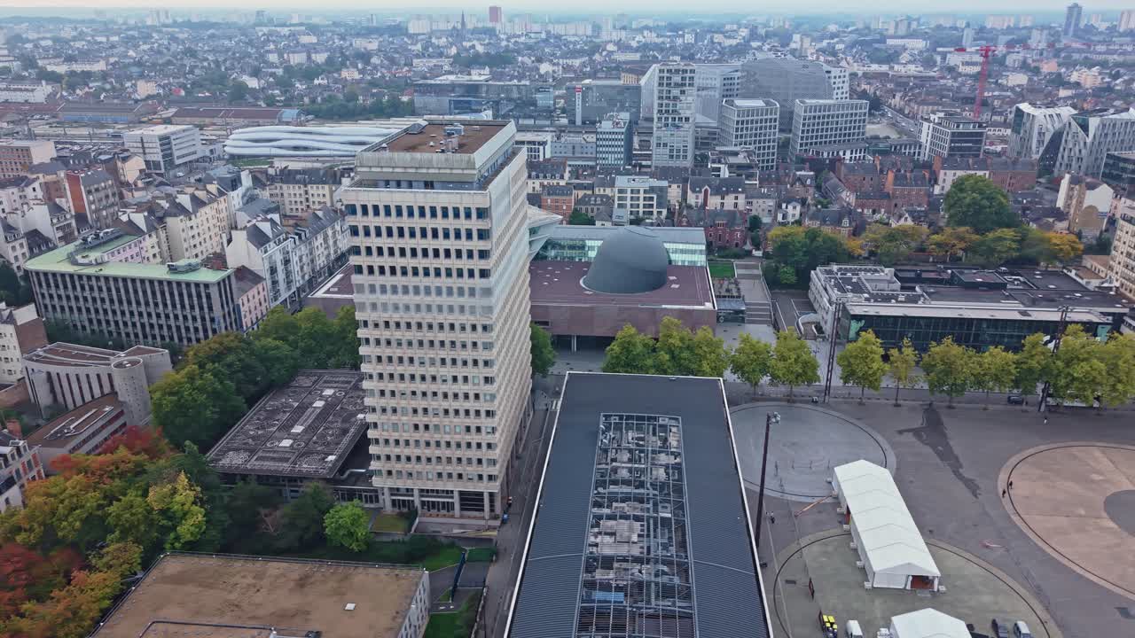 Drone performs a slight orbit and pan above Les Champs Libres, Colombier district of Rennes, showing nearby buildings and the train station in the background