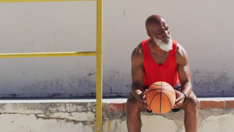 senior african american man exercising sitting and playing with basketball