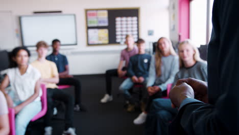 close up of male teachers hands as he faces class of high school students and teaches lesson