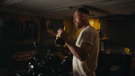 A-blond-guy-with-a-beard-in-a-white-T-shirt-takes-off-his-yellow-gloves-and-ends-his-day-in-a-motorcycle-workshop