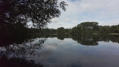 Panning-looking-across-a-still-reflective-lake-in-a-forest-in-England