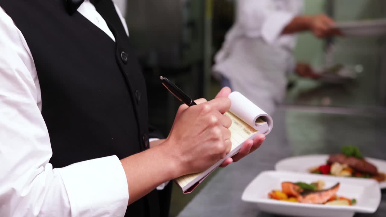 미소 짓는 웨이트리스가 메모장에 글을 쓰고 있다