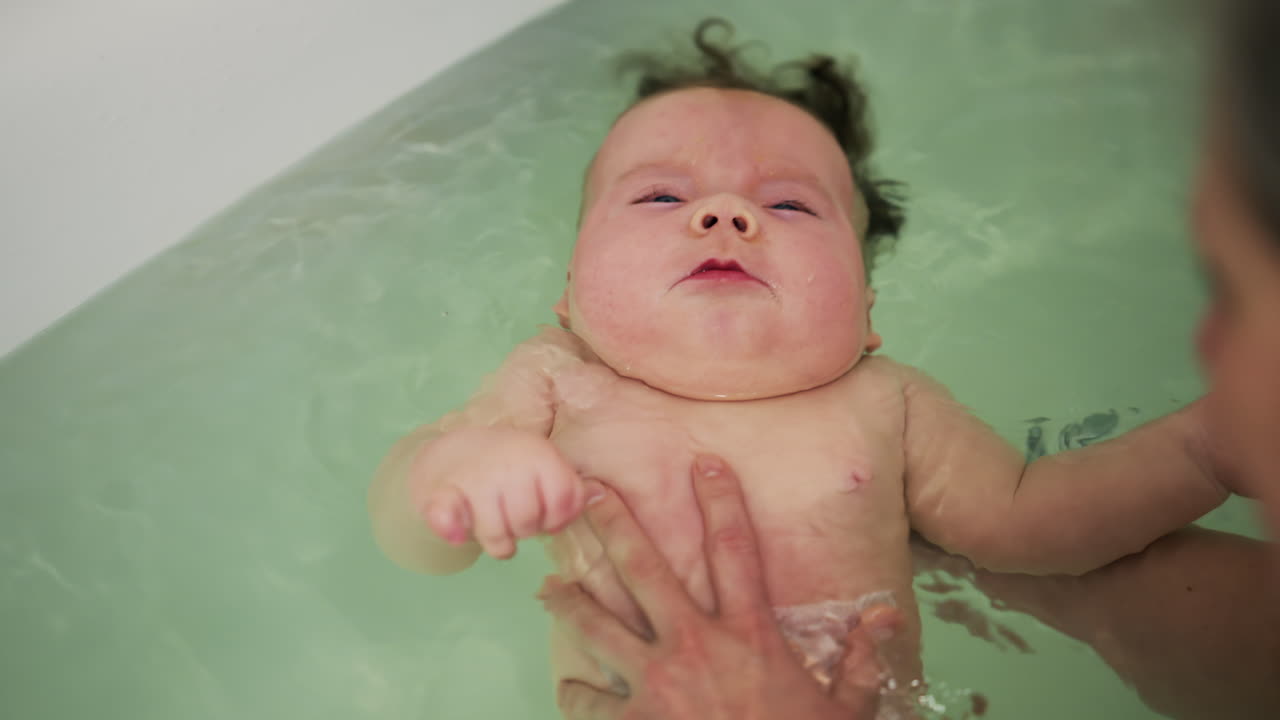 Baby enjoying bath time while being supported by a caregiver