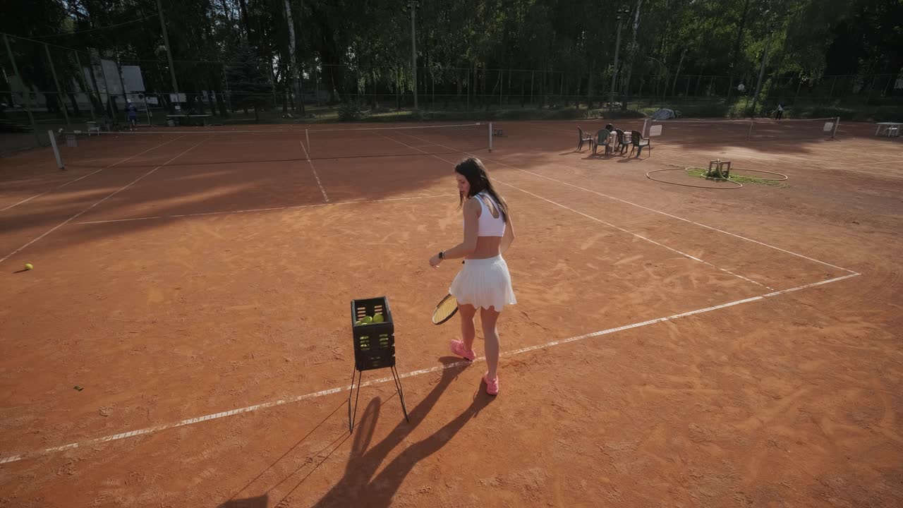 A young woman practicing tennis on an outdoor court with a coach. The coach provides guidance as the player works on her technique, perfecting her strokes in an athletic training session.