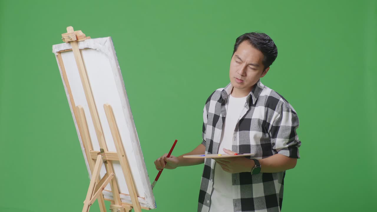 아시아 남성 예술가가 머리를 흔들고 머리가 아프고 캔버스에 기름색 페인트와 브러쉬를 그리며 그린 스크린 스튜디오에 있습니다.