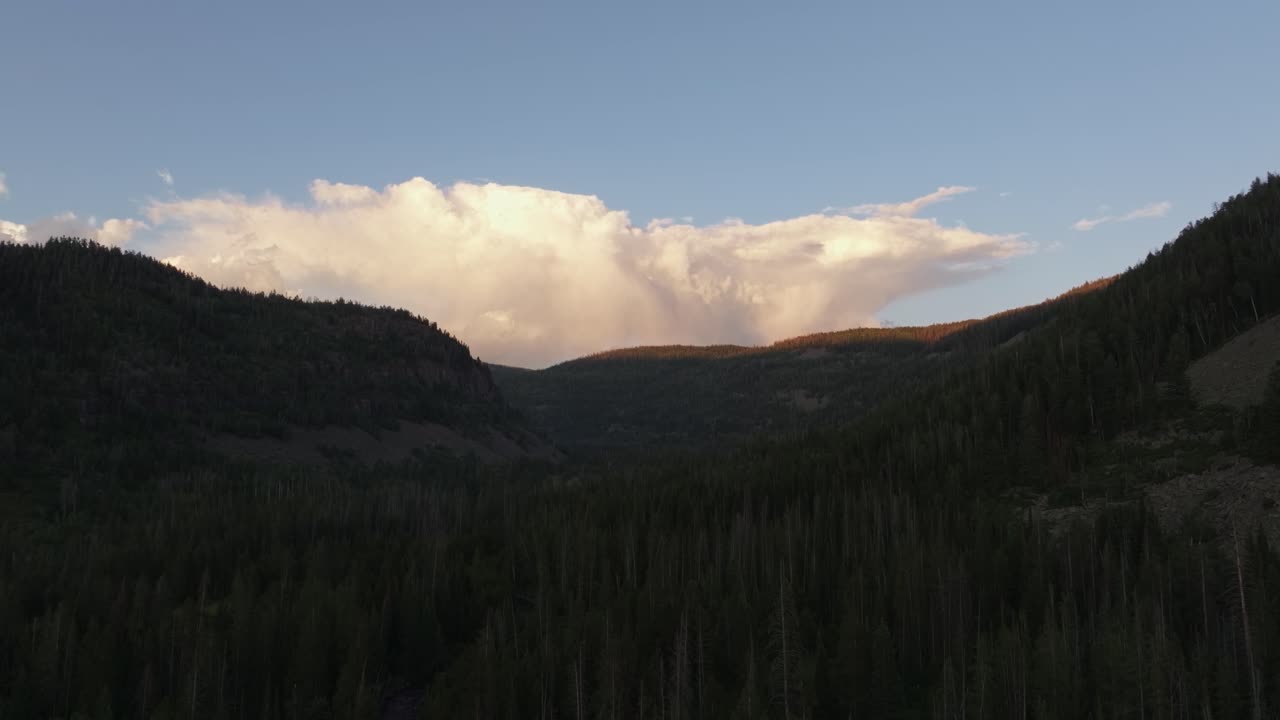 Drone rising wide shot of the Uinta-Wasatch-Cache National Forest in Utah during a summer sunset, pine trees, Provo River, and Bald Mountain and rain clouds rising above the valley