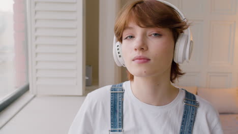 vista de cerca de una chica parada cerca de una ventana, luego se pone los auriculares y mira a la cámara