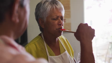 una pareja biracial preparando comida. una mujer disfruta del sabor de una cuchara.