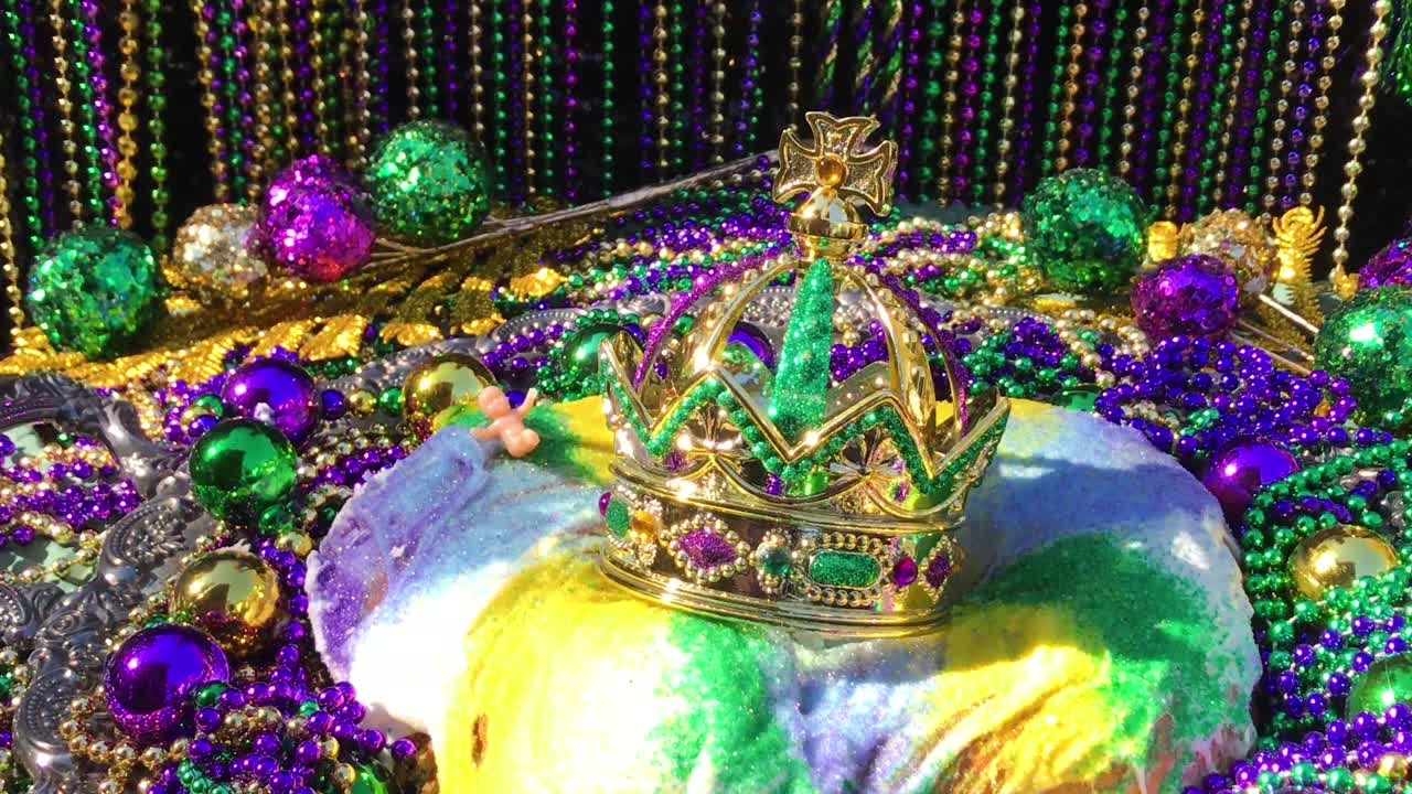 화려한 구슬로 둘러싸인 작은 아기와 왕관이 있는 마디 그라 킹 케이크 위로 움직이는 그림자