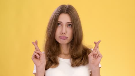 woman hoping with fingers crossed on yellow background